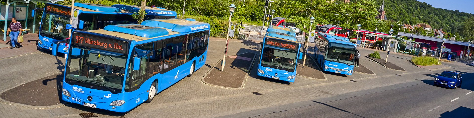 Vier blaue Busse der VRN-Flotte am Wertheimer Busbahnhof. Im Hintergrund ist die Westfrankenbahn zu sehen