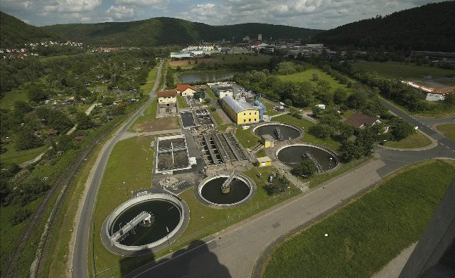 Zwei Fahrradfahrer schieben ihre Räder über die grüne Wiese entlang der Tauber. Im Hintergrund ist die Wertheimer Burg zu sehen.