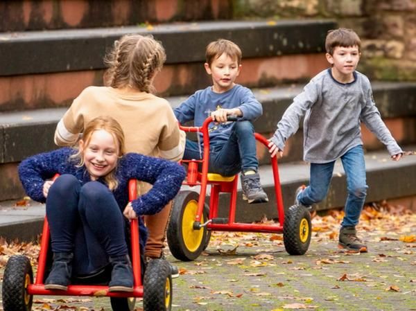 Vier Kinder beim Spielen im Freien mit zwei roten Dreirädern.