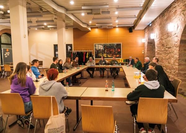 Teilnehmer der Dialogrunde "Jugend trifft Politik" sitzen gemeinsam mit den Verantwortlichen  an einem großen Tisch im Arkadensaal des Wertheimer Rathausese. 