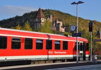 Eine rote Westfrankenbahn hält am Wertheimer Bahnhof. Im Hintergrund ist der Spitze Turm zu sehen.