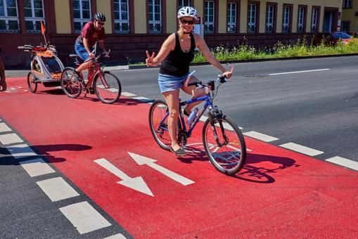 Zwei Fahrradfahrer überkreuzen die Straße an einer roten Querungshilfe