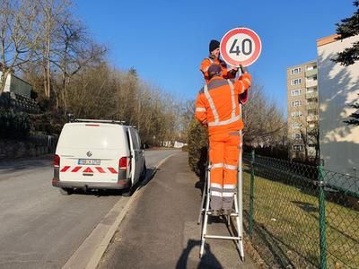 Zwei orange gekleidete Mitarbeiter des Wertheimer Bauhofs stehen auf einer Leiter. Sie montieren ein "Tempo 40" Schuld im Stadtteil Wartberg. Im Hintergrund ist das weiße Auto der Bauhofmitarbeiter zu sehen. 