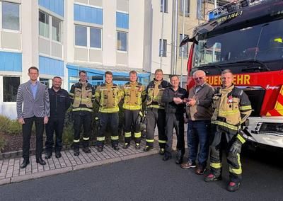 Vertreter des Unternehmens und Feuerwehrleute vor dem Firmengebäude