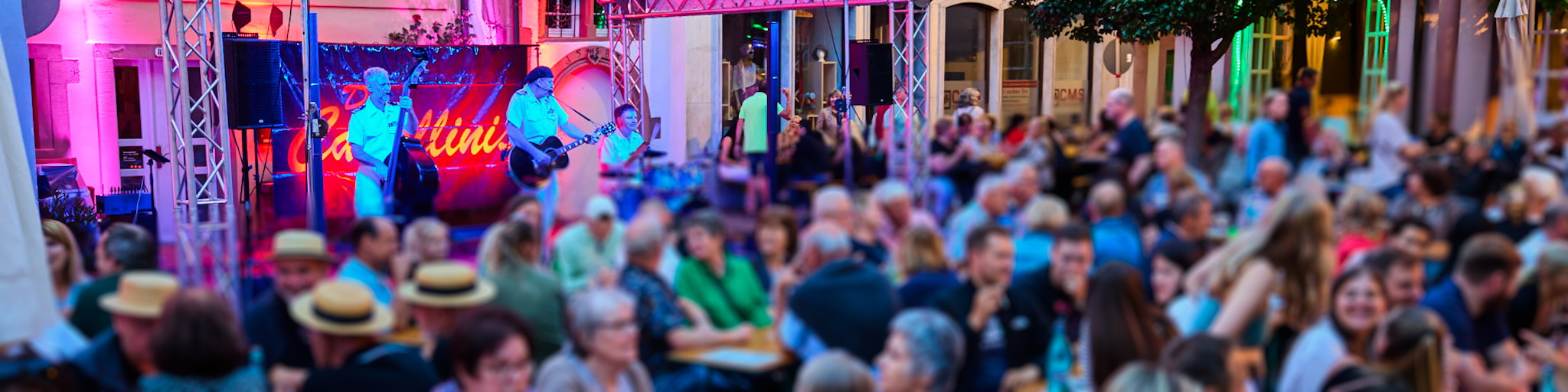 Viele Menschen sitzen bei stimmungsvoller Beleuchtung auf einem Wertheimer Platz und hören einer Bnad zu. Das Foto stammt vom Altstadtfest.