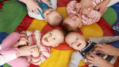 Vier Babys liegen im Kreis auf Babydecke, Ansicht von oben