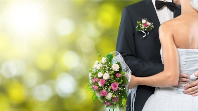 Symbolbild zur Inhaltsseite Heiraten: Der Bräutigam umarmt seine Braut, die man nur von hinten sieht. 