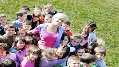 Gruppe von Kindern auf grünem Rasen, in der Mitte Erzieherin.