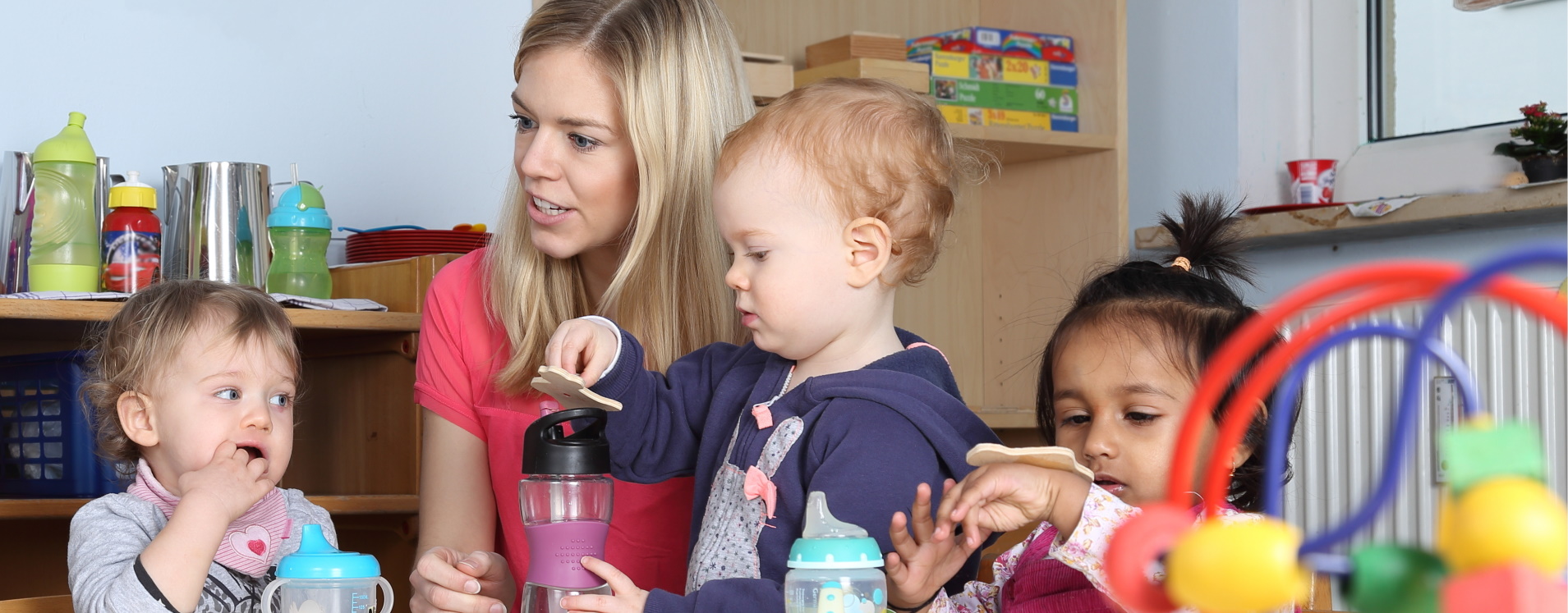 Eine blonde Frau (Erzieherin) mit drei Kleinkindern.