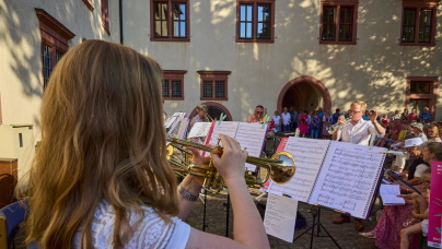 EIn Mädchen spielt Trompete. Sie ist von hinten zu sehen. Vor ihr befindet sich ein Notenständer mit Notenblättern.