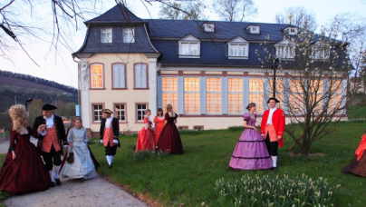 Das Schlösschen im Hofgarten. Ebenfalls zu sehen sind Männer und Frauen in Roben des 19. Jahrhunderts.
